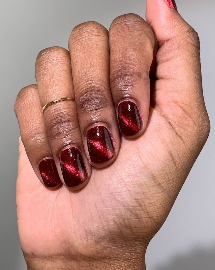 Mão de pele preta, com anel em prata e unha quadrada olho de gato em vermelho