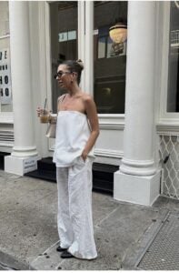 Mulher jovem de pele clara. Ela está usando uma blusa sem mangas e calça.