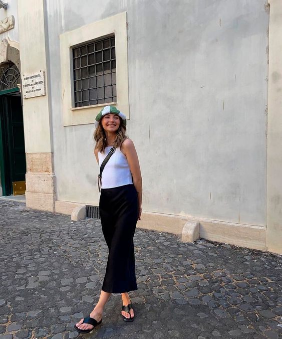 Mulher usando chapéu, regata branca, saia longa preta e chinelo