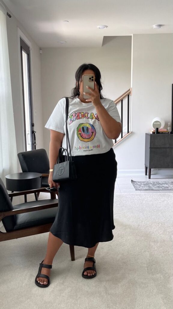 Mulher jovem com camiseta branca estampada e saia acetinada preta.