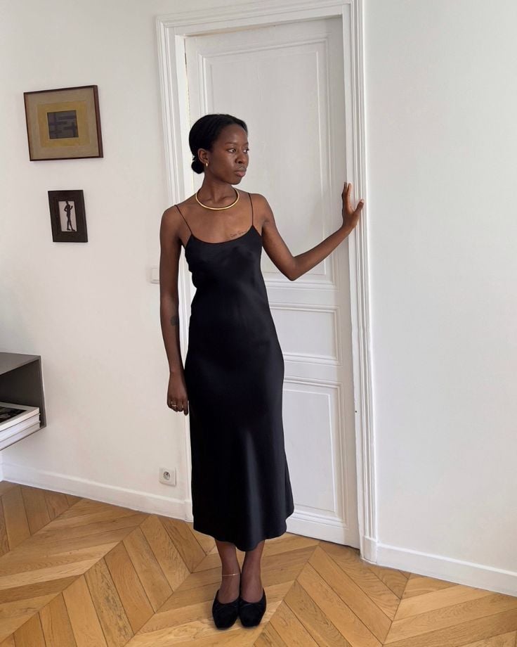 Mulher jovem e magra de pele negra usando vestido acetinado preto. Look de ano-novo com vestido de cetim preto