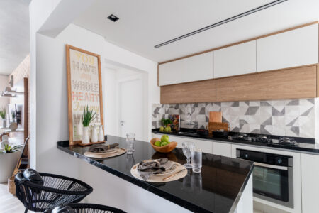 Cozinha com móveis brancos e em MDF que remete à madeira, com bancada preta, quadro e mesa posta