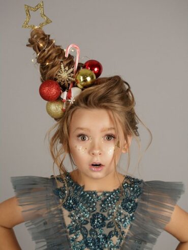 Menina branca e loira, usando vestido de festa com detalhes de pedraria em cor azul, usando cabelo maluco de árvore de Natal.
