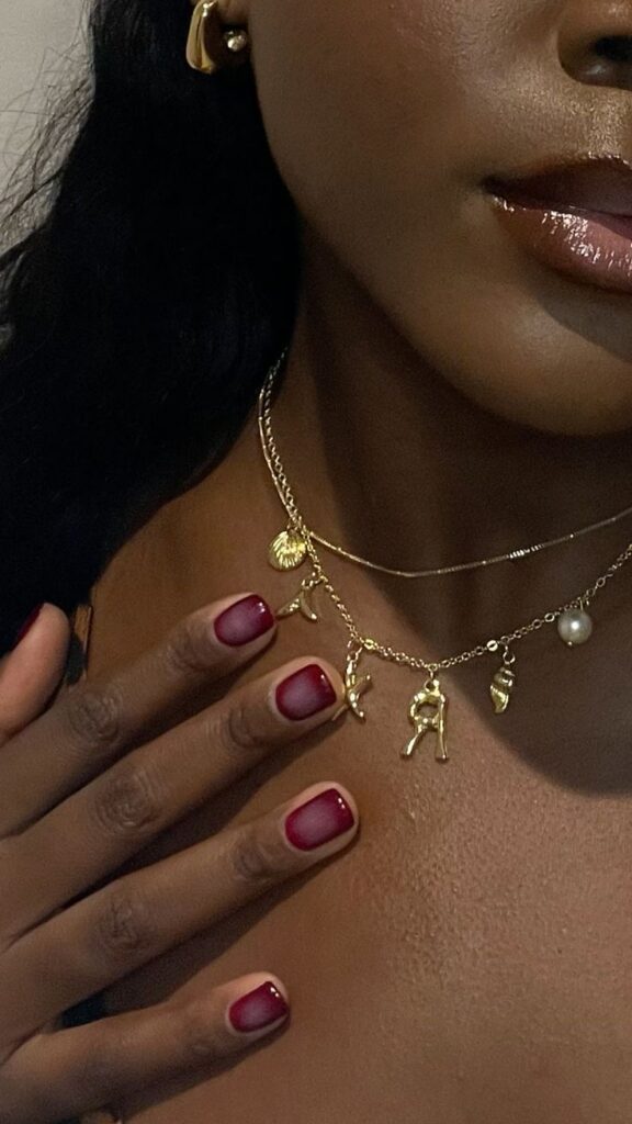 Mão de pele negra, com unha curta e quadrada usando esmalte vinho, com nail art de aura nails