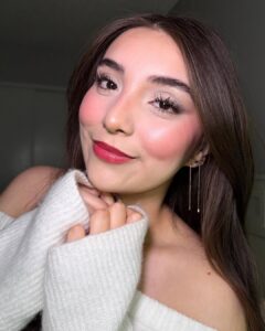 Mulher de pele clara, com blusa branca, cabelo escuro e blush candy cane