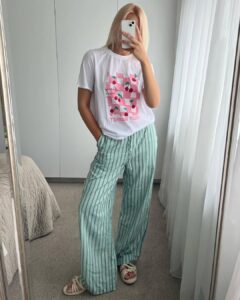 Mulher magra e de pele clara, com cabelo loiro solta, blusa estampada, calça de linho listrada e calçado off-white