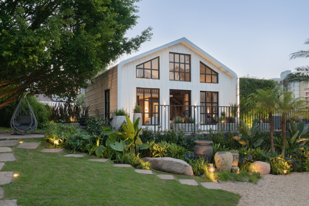 Casa em estilo farm house e paisagismo com pedras, vasos e plantas