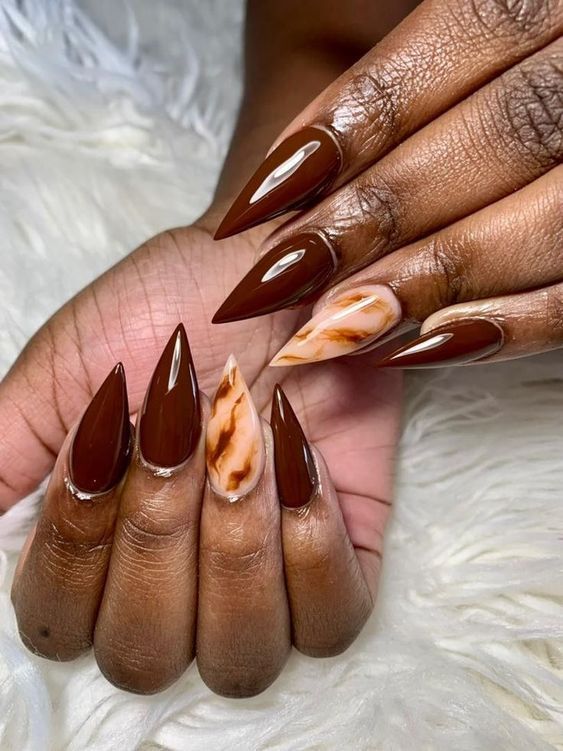 Mãos de pele preta, com unha stiletto marrom e e unha do dedo anelar marmorizada