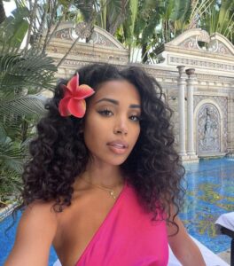 Mulher de pele preta, com vestido rosa, acessório em dourado e cabelo cacheado escuro