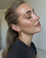 Mulher de pele clara, com blusa preta, cabelo meio-preso e pele hidratada