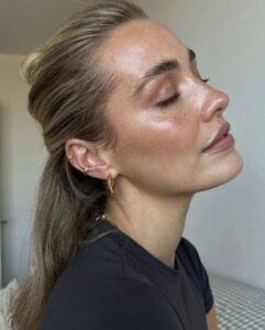Mulher de pele clara, com blusa preta, cabelo meio-preso e pele hidratada