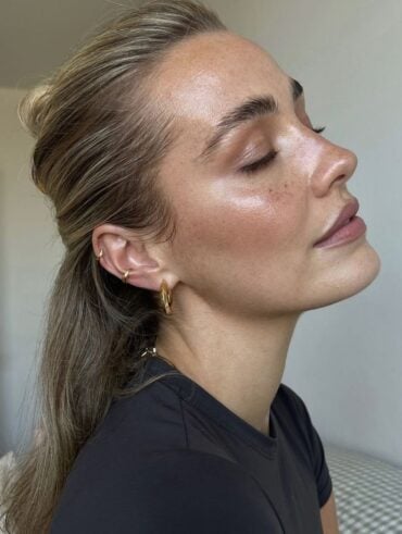 Mulher de pele clara, com blusa preta, cabelo meio-preso e pele hidratada