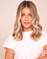 Mulher com corte de cabelo curto, no estilo long bob, castanho e com luzes loiras. Usa blusa branca básica