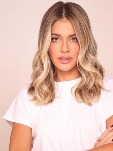 Mulher com corte de cabelo curto, no estilo long bob, castanho e com luzes loiras. Usa blusa branca básica