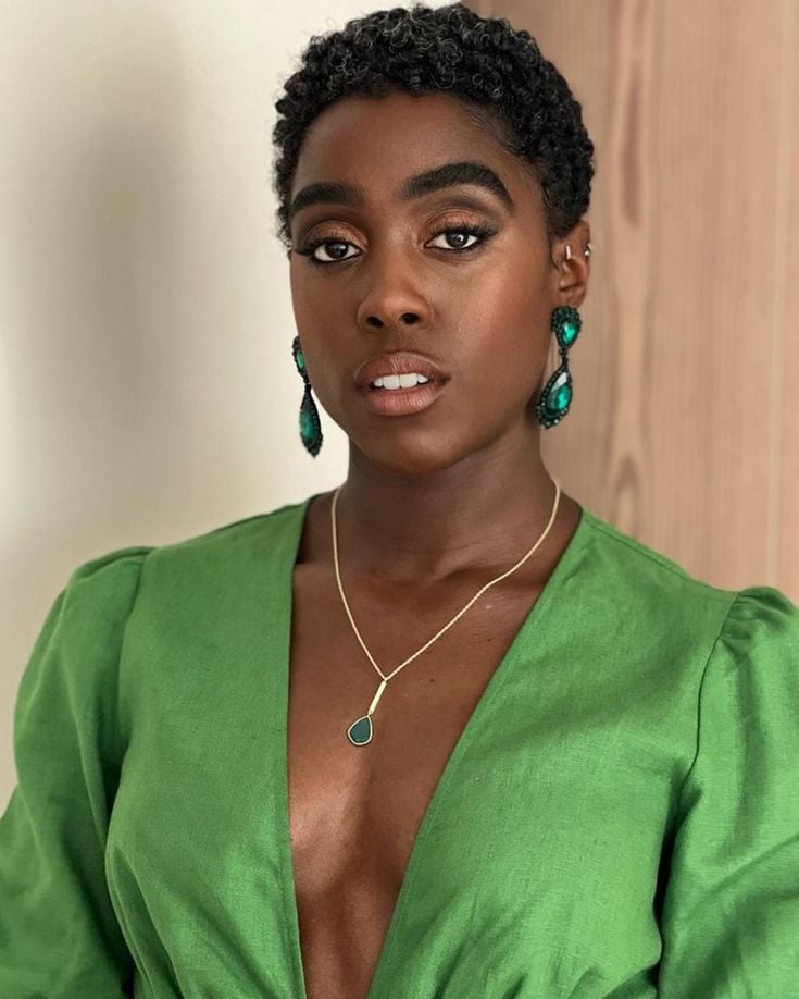 Mulher de pele clara, com vestido verde, acessórios em dourado e verde e cabelo pixie com volume