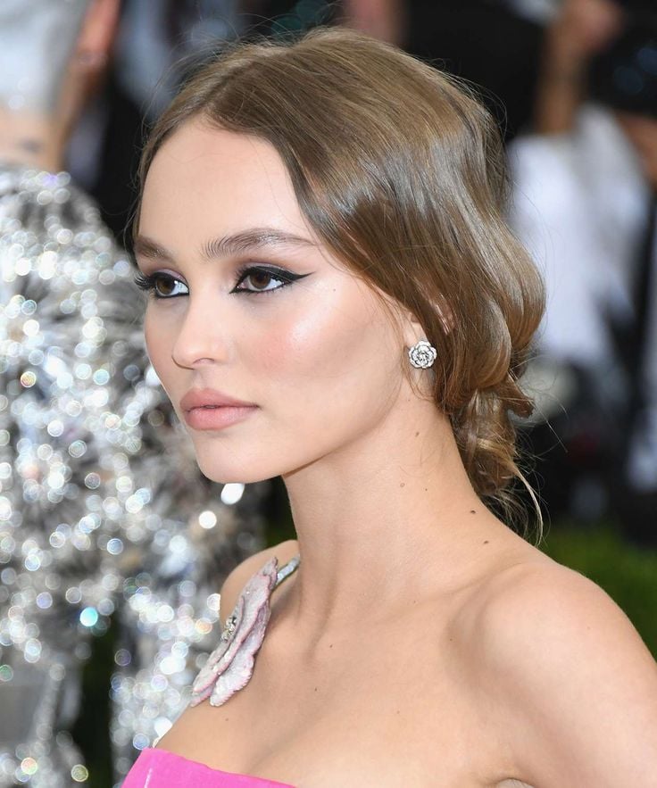 Lily-Rose Depp, com vestido rosa, cabelo preso e olhos amendoados com delineado