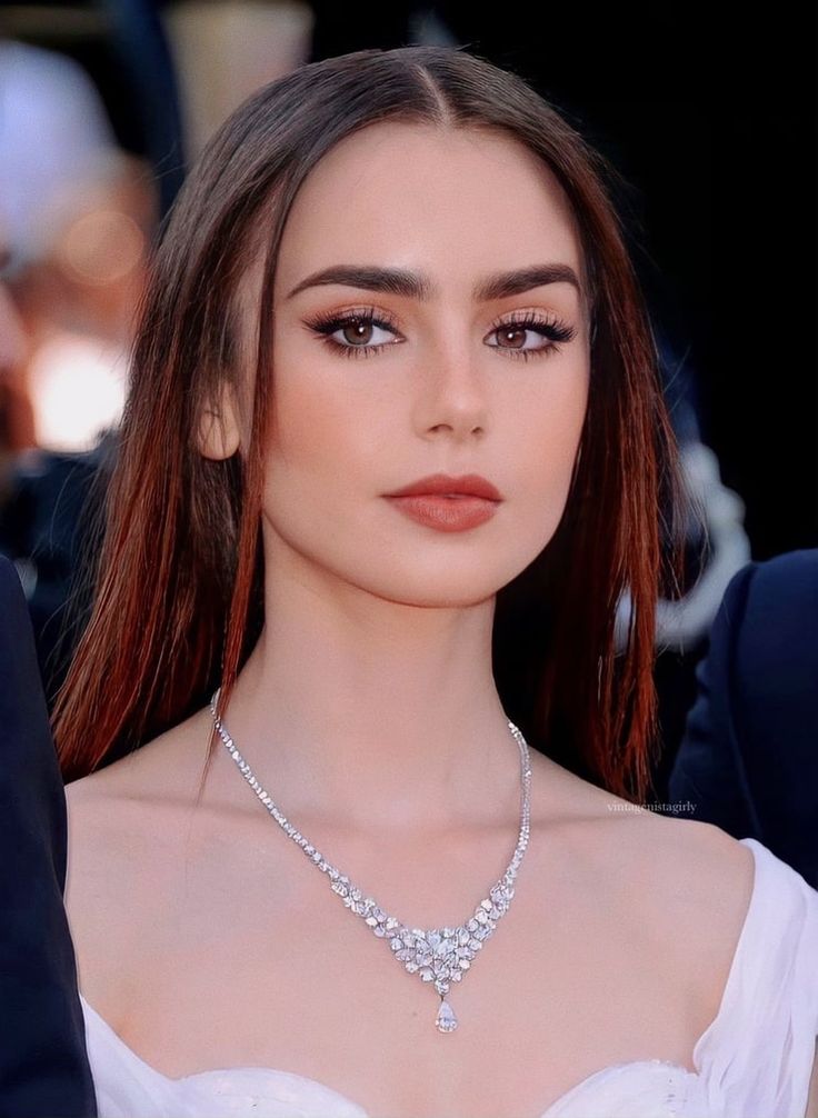 Lily Collins, com vestido branco, acessórios em prata, cabelo liso e delineado para olhos redondos