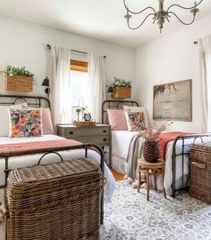 Quarto com duas camas de ferro, almofadas com flores e cestos de vime