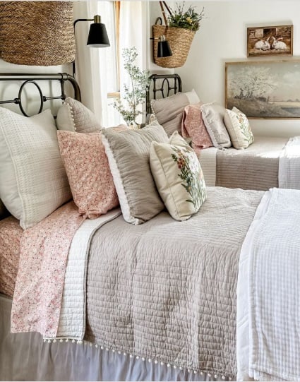 Quarto com camas duplas de ferro, roupa de cama neutro e cesto de fibra natural