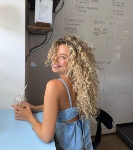 Mulher de pele clara, com vestido jeans e cabelo loiro cacheado