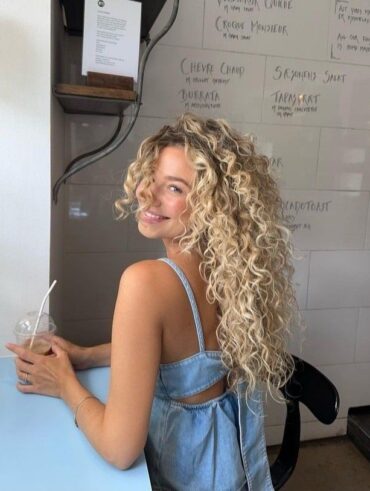 Mulher de pele clara, com vestido jeans e cabelo loiro cacheado