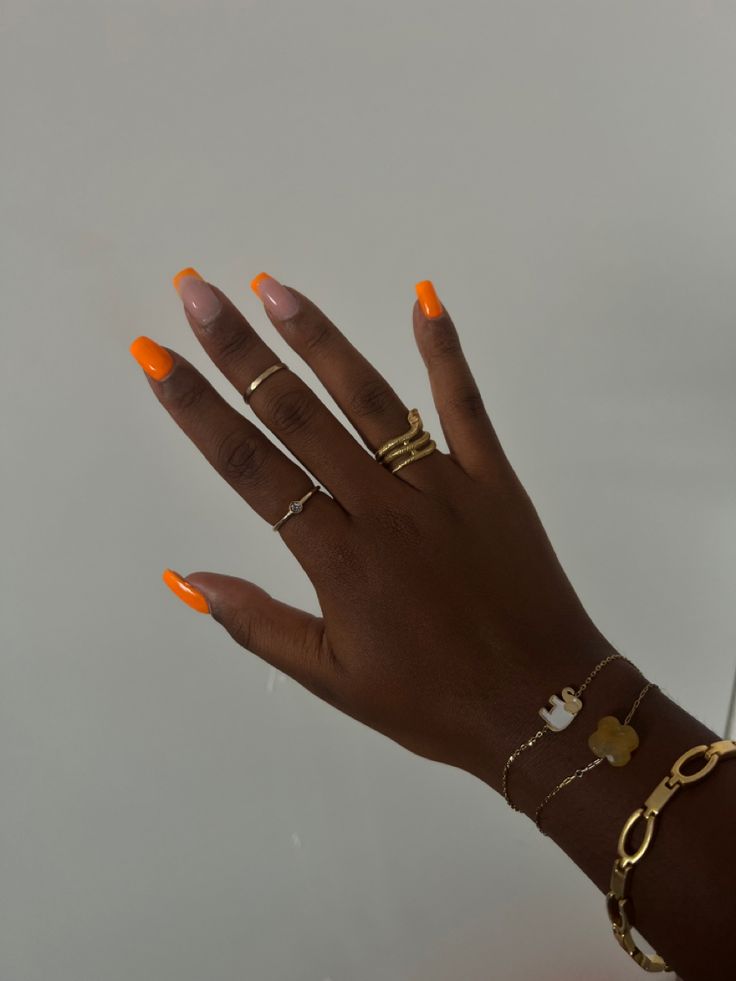 Mão de pele preta, com acessórios em dourado e unha quadrada laranja neon com francesinha