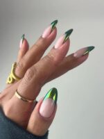 Mão de ple clara, com acessórios em dourado e unha amendoada com francesinha verde cromada