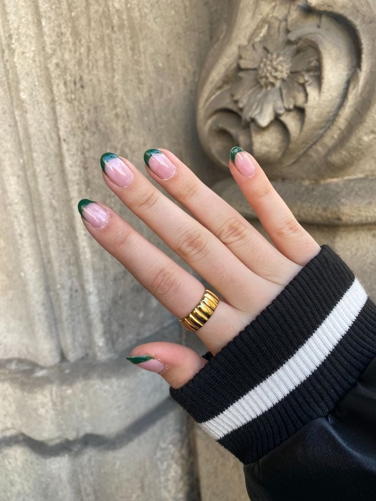 Mão de pele clara, com anel em dourado e unha amendoada com francesinha verde-esmeralda