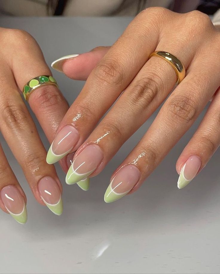 Mãos de pele clara, com anéis em dourado e unha amendoada com francesinha verde-claro 