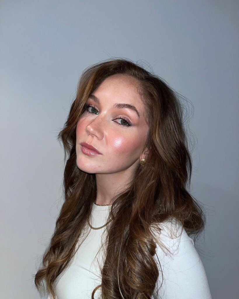 Mulher de pele clara, com cabelo médio, blusa branca e glazed makeup