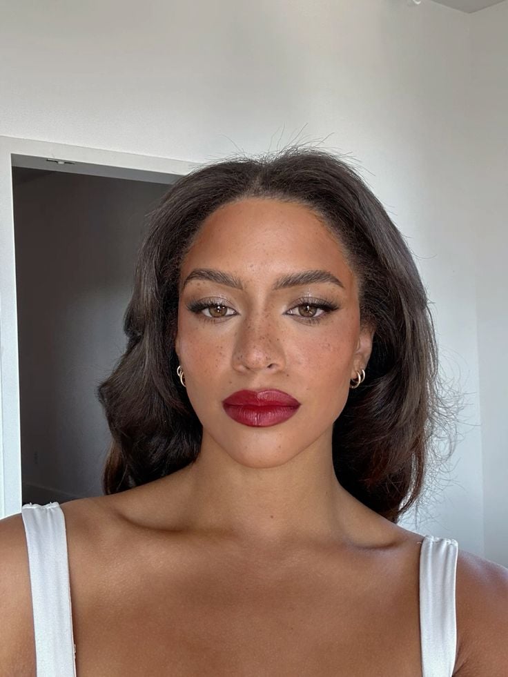 Mulher de pele negra, com cabelo escuro solto, maquiagem simples e regata branca 