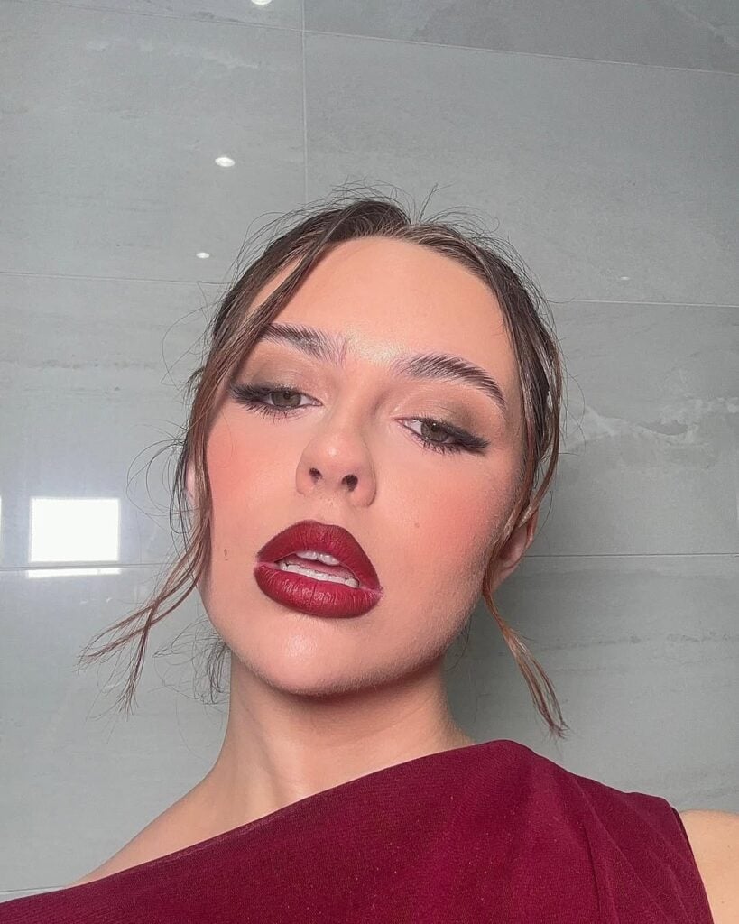 Mulher de pele clara, com cabelo meio preso, roupa vermelho-escuro e maquiagem com batom vinho