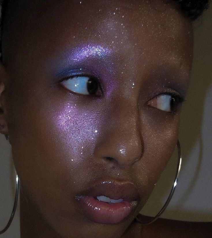 Mulher com pele preta, brinco de argola e maquiagem com efeito aura e brilho