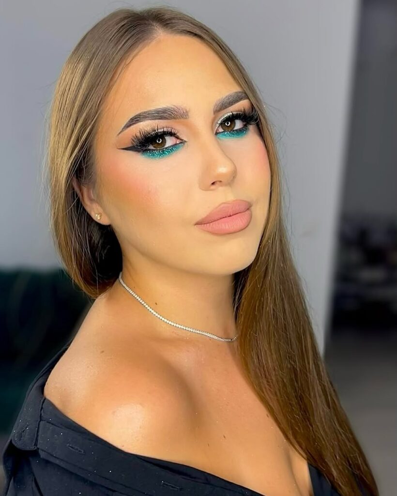 Mulher de pele clara, com roupa preta, cabelo loiro-escuro e maquiagem com delineado invertido colorido