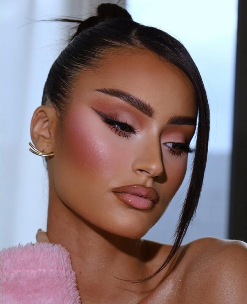 Mulher de pele média, com cabelo escuro preso e maquiagem em tons de rosa
