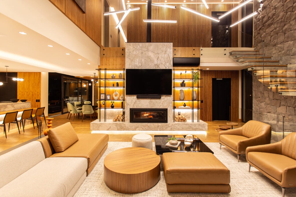 Sala de estar com sofá e poltronas em couro caramelo, lareira e pendentes