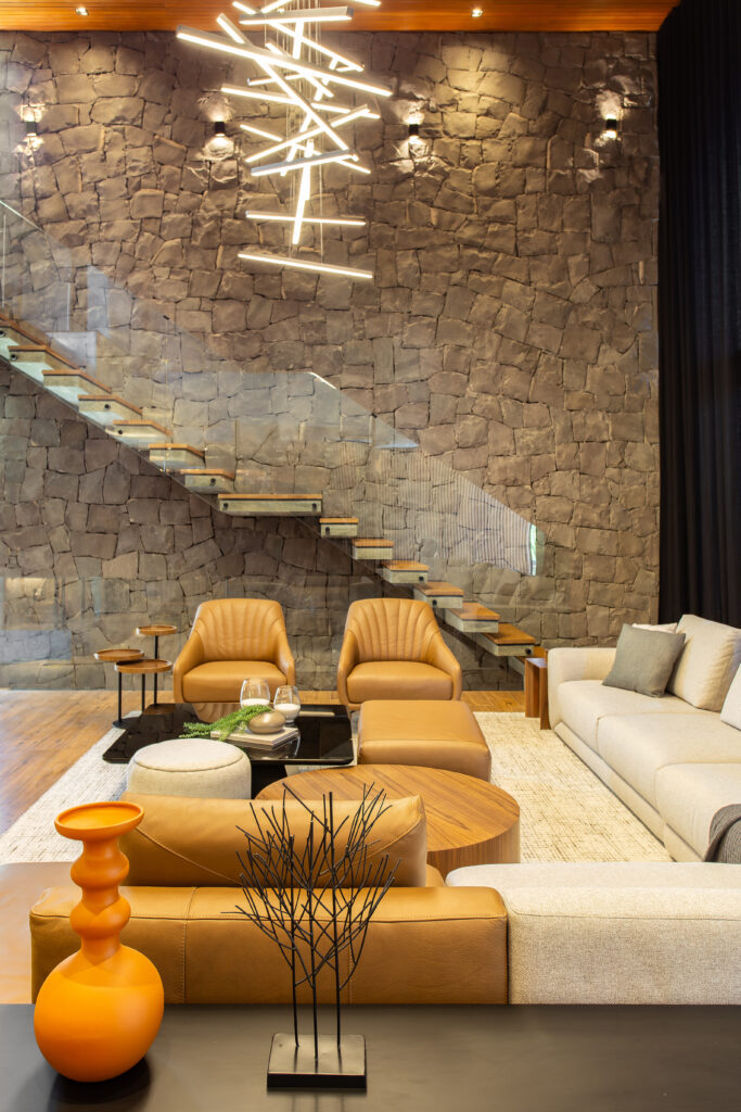 Sala de estar com parede revestida de pedra e escada com madeira e vidro