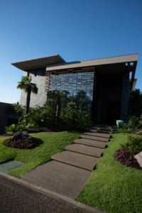 Fachada de casa com grama, parede com vidro e revestimentos em concreto cinza