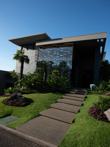 Fachada de casa com grama, parede com vidro e revestimentos em concreto cinza