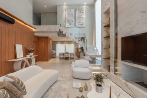 Ambiente integrado com sala de estar com lareira, sala de jantar, detalhes amadeirados e uma escada de pedras com vidro