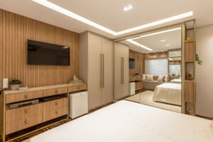 Quarto com estilo sofisticado, cama de casal, mesas de cabeceira e guarda-roupa com espelho, ripado na parede e gesso com sanca iluminada