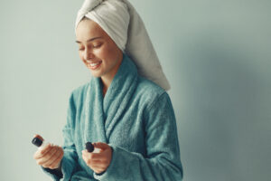 Mulher com toalha na cabeça e roupão, fazendo rotina de skincare e cuidado com a pele
