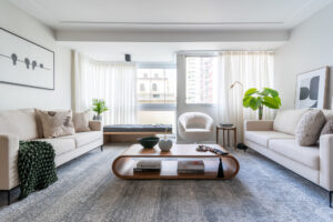 Sala de estar com janelas amplas, poltrona, sofás brancos e mesa de centro com layout curvo