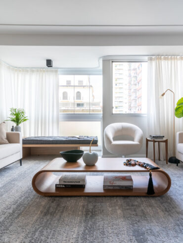 Sala de estar com janelas amplas, poltrona, sofás brancos e mesa de centro com layout curvo