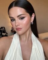 Selena Gomez, com vestido branco, cabelo solto e maquiagem iluminada