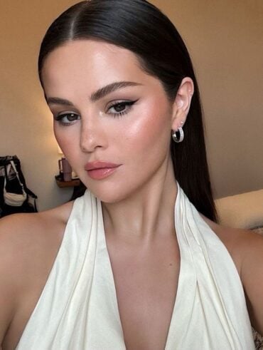Selena Gomez, com vestido branco, cabelo solto e maquiagem iluminada