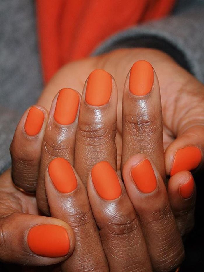 Mãos de pele preta, com unha amendoada laranja neon com acabamento fosco
