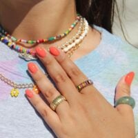 Mão de pele clara, com acessórios coloridos e unha amendoada coral