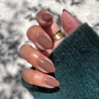Mão de pele média, com acessórios em dourado e unha amendoada marrom suave