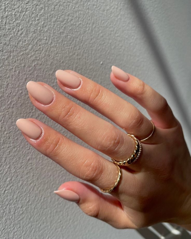 Mão de pele clara, com anéis em dourado e unha amendoada nud e